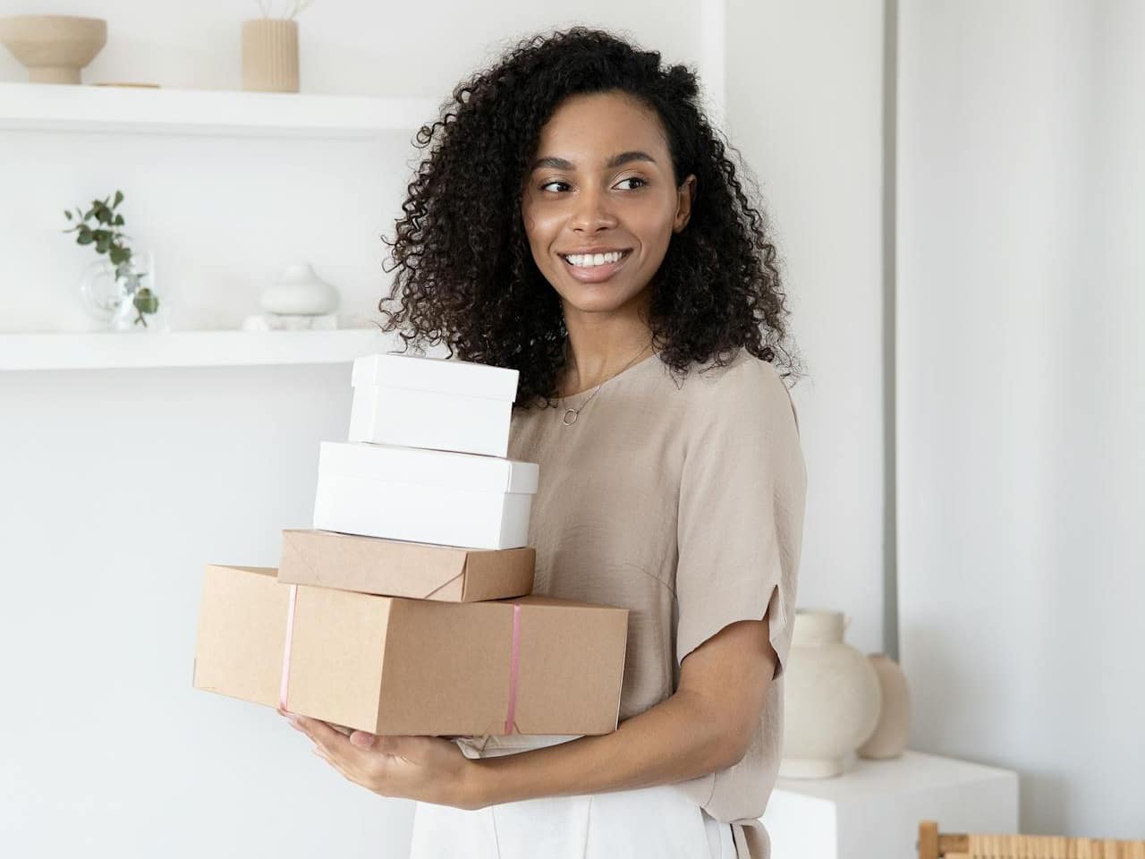 Brown woman holding 4 boxes, the two bottom ones are brown and the top two are white