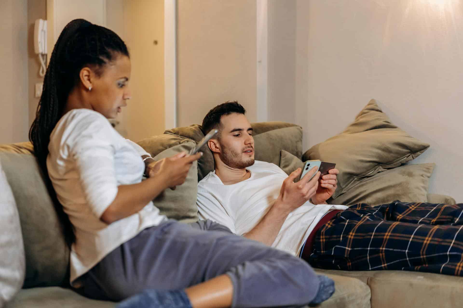 A man and woman sitting on a couch looking at phones.