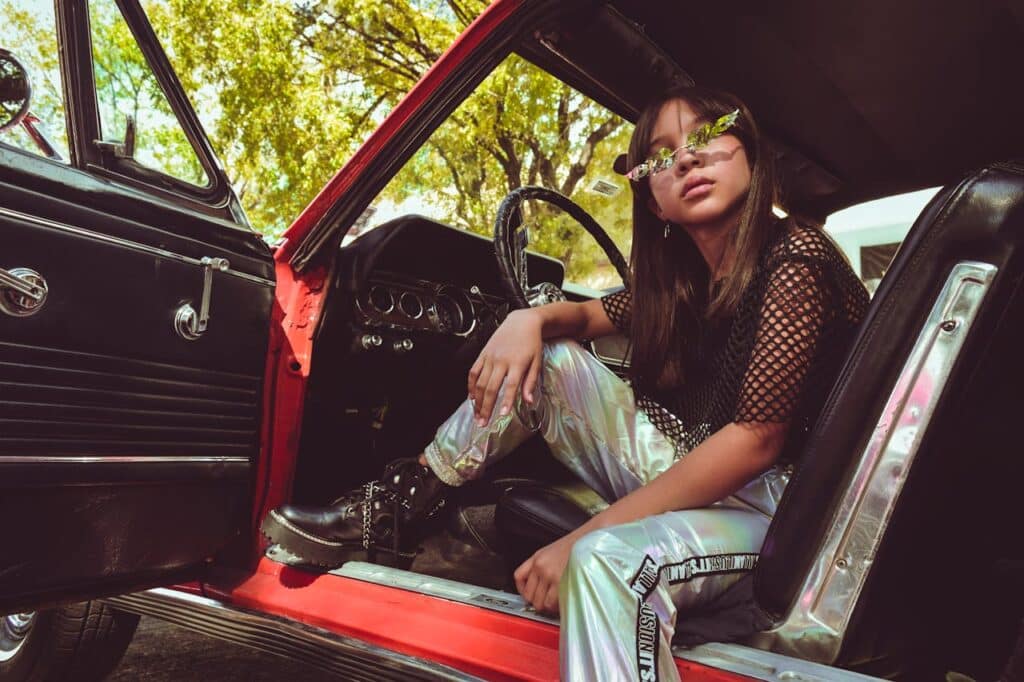 A girl sitting in the front seat of a car wearing Y2K fashion.